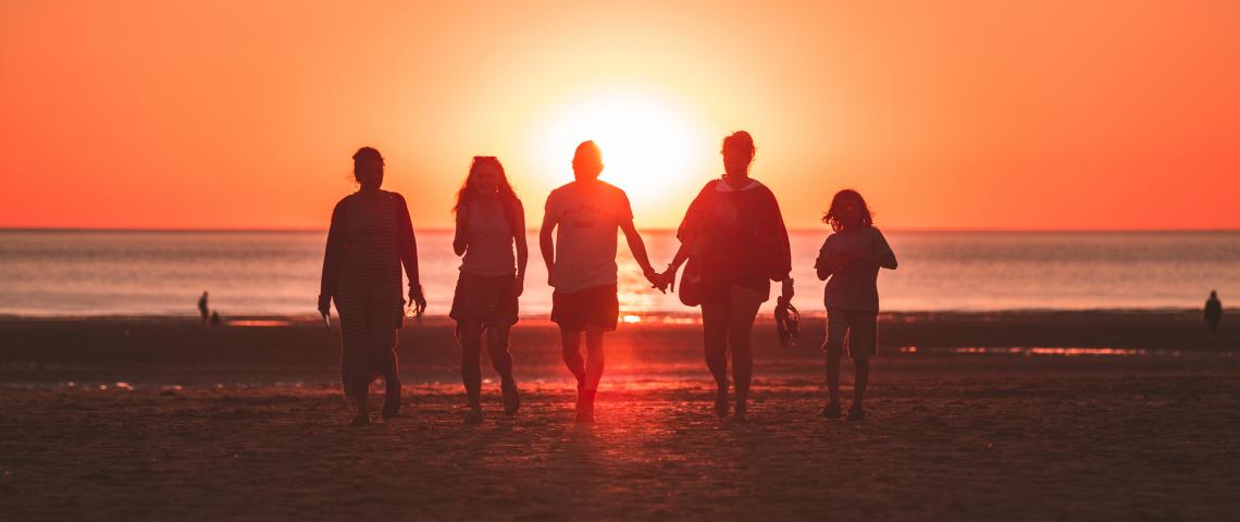 Fem personer går på en strand i solnedgången. 