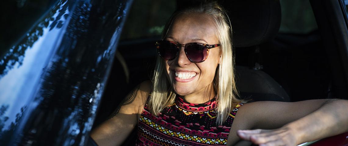 En glad tjej med solglasögon som sitter i en bil